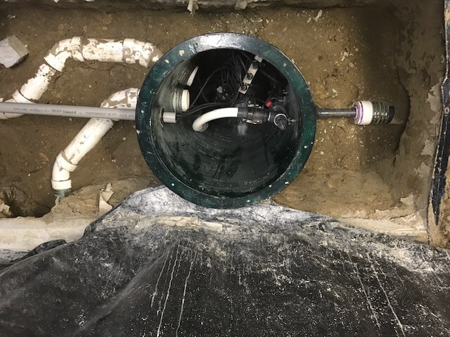 A buried septic tank with plumbing pipes connected to it, showing the lid and some internal equipment inside the tank.
